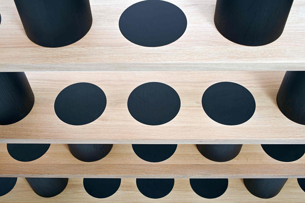 Ansicht des Bücherregals von oben mit kreisförmig eingelassenen schwarzen Zylindern aus massivem Holz