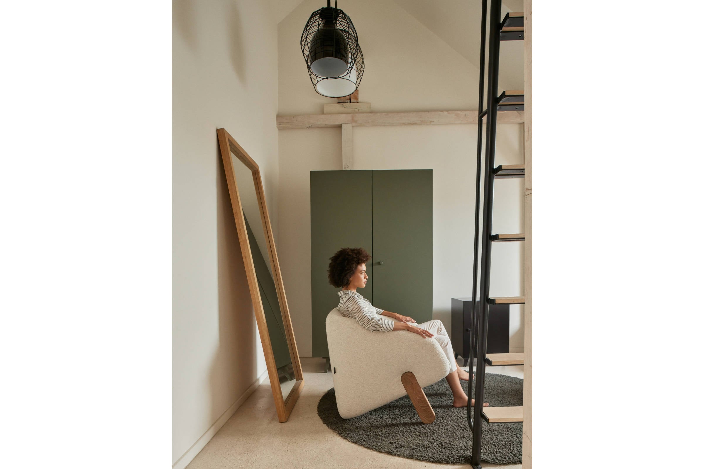 Person sitzt entspannt im Sessel, minimalistisches Ambiente mit Spiegel und Schrank